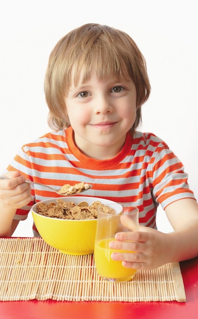 Фото Маленький мальчик в полосатой футболке ест мюсли и пьет апельсиновый сок