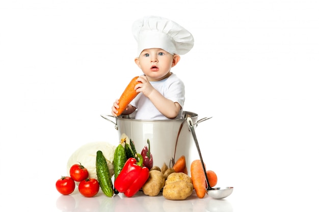 Маленький мальчик в шляпе шеф-повара с ковшом, кастрюлей и овощами