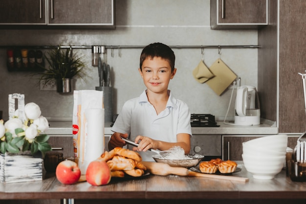 写真 生地を作る台所の小さな男の子。男の子は台所でお母さんを助けます。
