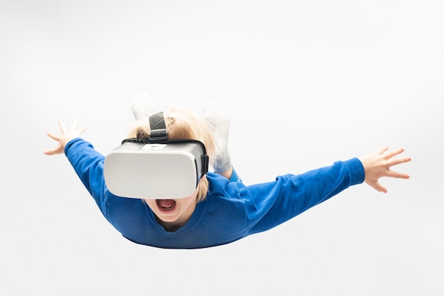 Фото Маленький мальчик в очках виртуальной реальности падает с высоты. белая стена. видеоигры.