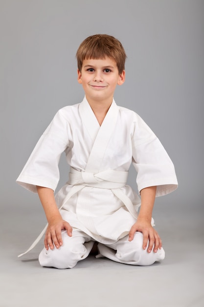 Фото Маленький мальчик в белом кимоно занимается карате