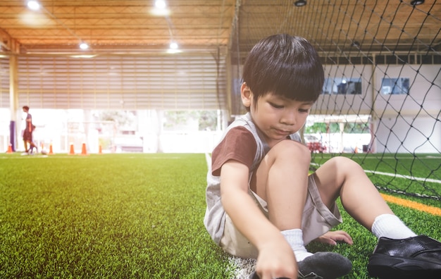 小さな男の子がサッカートレーニングのために靴を変えている