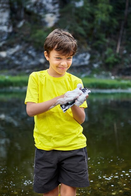 小さな男の子が川で携帯電話を洗っている間に破壊している、彼は笑っている。