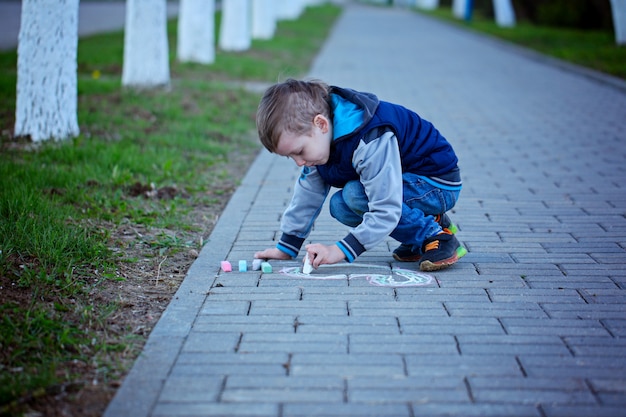 Little boy is drawing on asphalt in spring park.