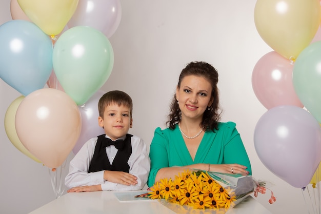 Маленький мальчик-первоклассник на белом фоне с мамой с шарами и цветами