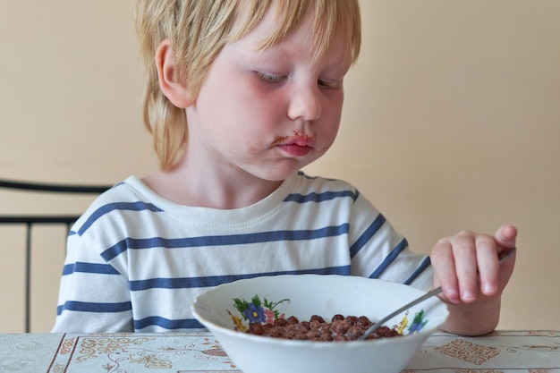 小さな男の子はミルクとチョコレートボールで朝食を食べています