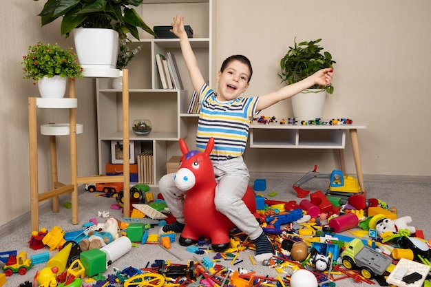 A little boy is jumping on an inflatable rubber donkey among the mess in the children's room