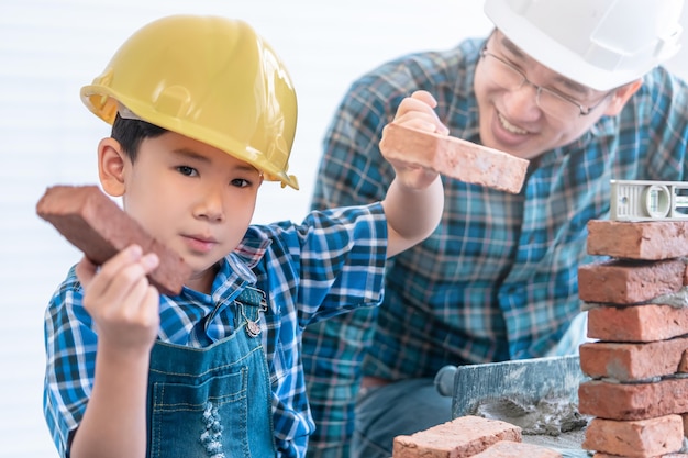 Little boy is learning how to lay down brick work from his\
builder father in vintage tone