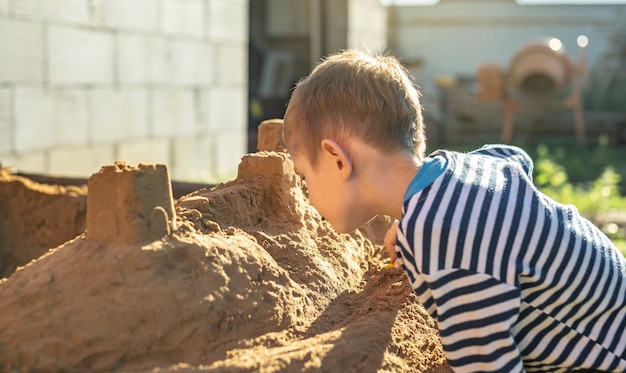 Little boy is playing outside near the house and building a sand castle