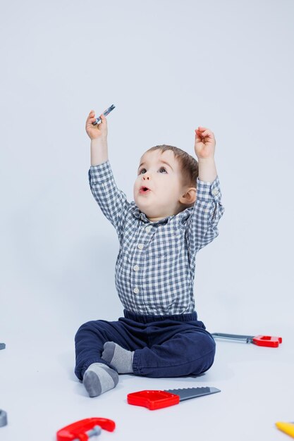 小さな男の子は、白い背景にビルダーのツールのおもちゃセットで遊んでいます。子供のプラスチック製のおもちゃ