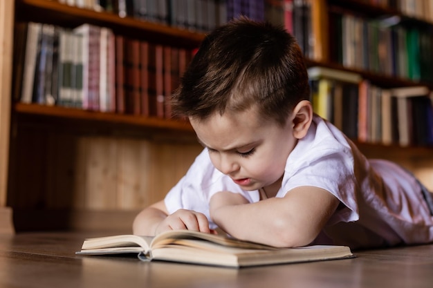 little boy is reading a book in the library at home