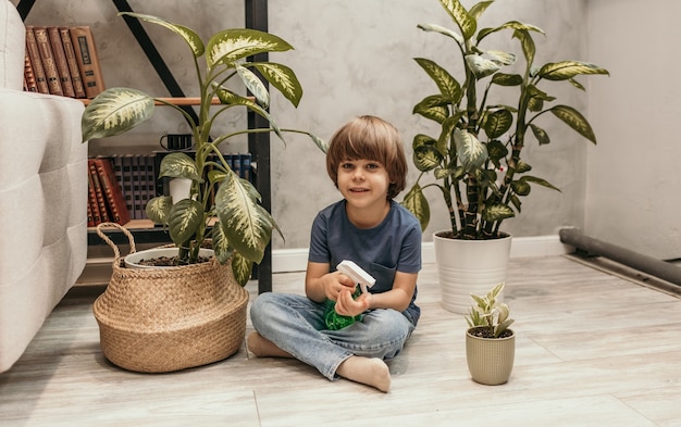 Маленький мальчик сидит на полу в комнате с растениями и держит опрыскиватель