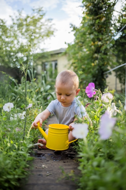 A little boy is sitting in the garden with a yellow watering can