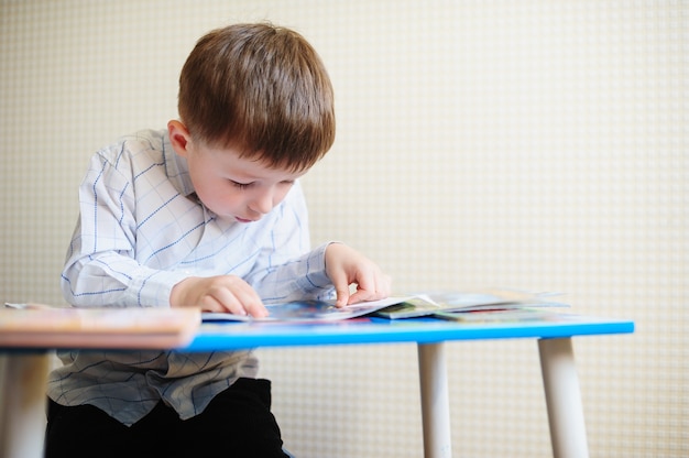 小さな男の子は彼の机に座って本を読みます。