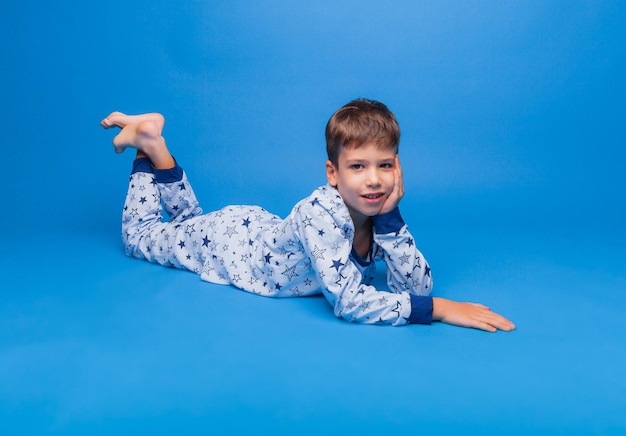 A little boy is sitting in pajamas on a blue background the concept of healthy sleep pajamas made of natural material for children