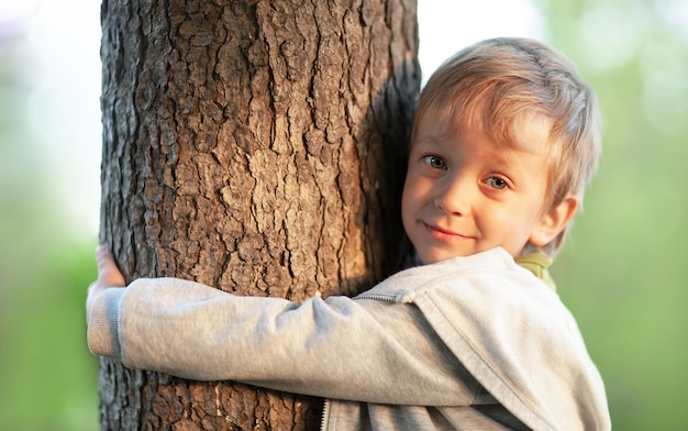 the little boy is smiling hugging the tree with his hands