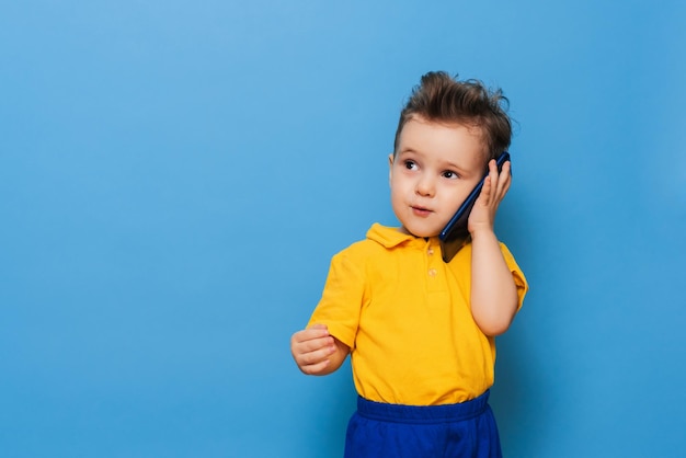 小さな男の子が携帯電話で話している。青い背景のスタジオ写真。