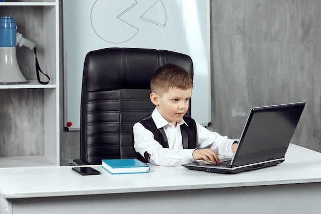 A little boy is working on a laptop in the office