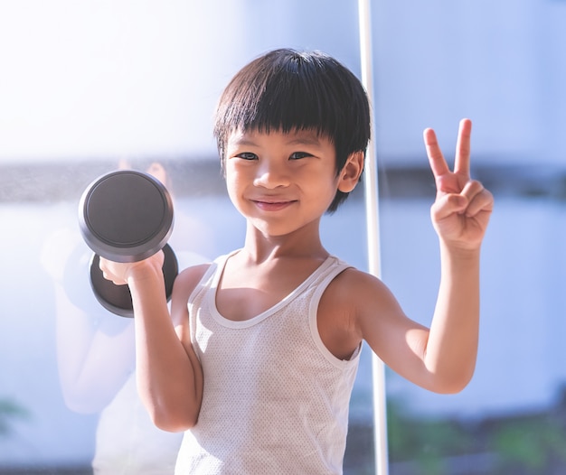 Little boy is working out with dumbbell by the windows city.