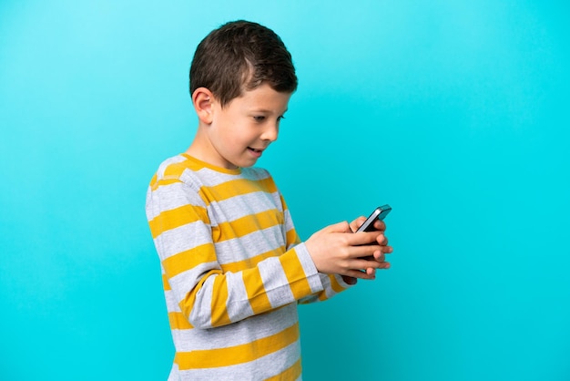 Little boy isolated on blue background sending a message or email with the mobile