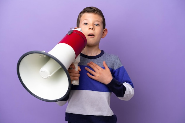 Photo little boy isolated on purple background shouting through a megaphone with surprised expression