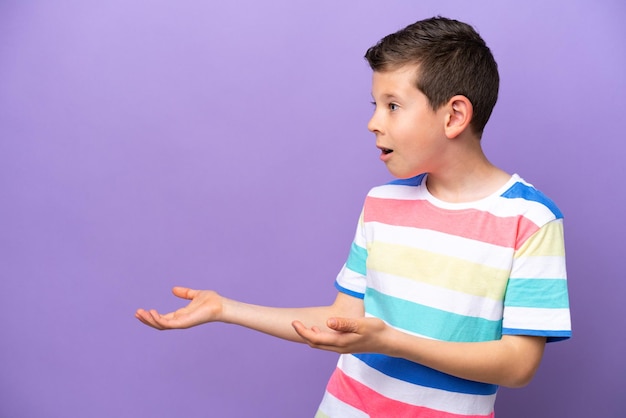 Little boy isolated on purple background with surprise expression while looking side