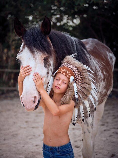 Little boy in jeans and bonnet stroking horse trying to feel emotions of his best friend