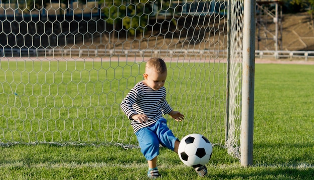 Little boy kicking a ball out of the goals while playing soccer on a lush green field