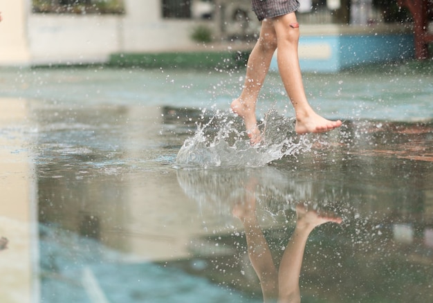 Little boy kicking ball in the water logging on the street