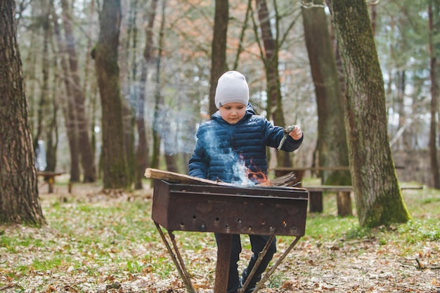 Little boy kid put branches in fire into grill