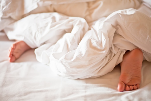 Little boy kid sleeping show feet under out of white blanket
