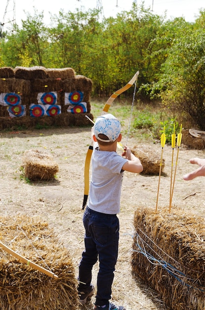 Маленький мальчик, ребенок с луком и стрелой, нацеленный на стрельбу из лука в парке, вид сзади. Открытый спорт