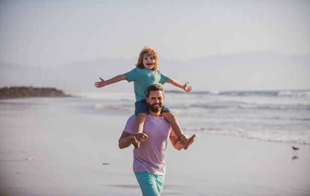 Little boy kid with daddy carrying him on shoulders father giving son ride on back outside concept o