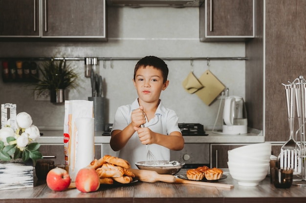 生地を作る台所の小さな男の子。男の子は台所でお母さんを助けます。