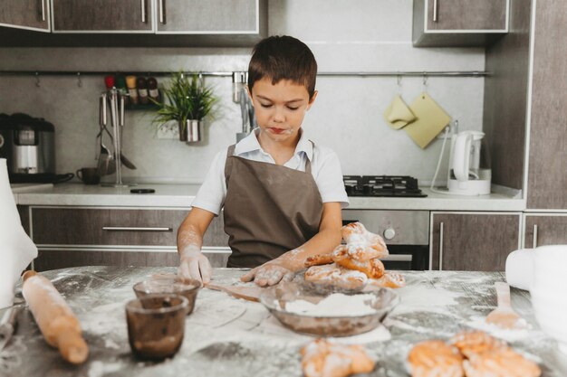 生地を作る台所の小さな男の子。男の子は台所でお母さんを助けます。