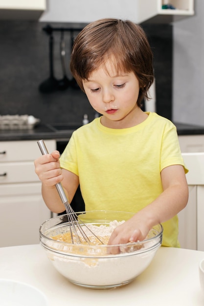 Little boy kneading dough with a whisk in the kitchen and smiling time with children at home