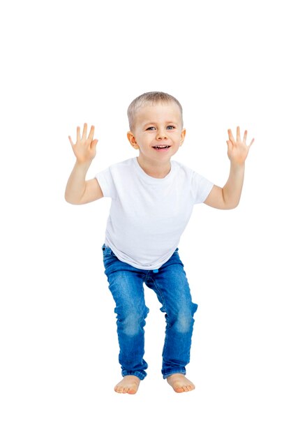 A little boy laughs and jumps with his arms outstretched funny Child in a white Tshirt and jeans Activity and energy Isolated on a white background Vertical