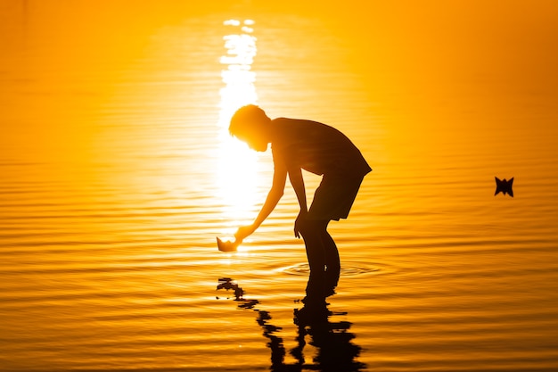 Little boy launching paper ships from riverside