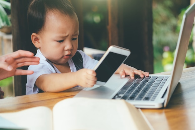 little boy learning with mobile phone, laptop, tablet, and book.