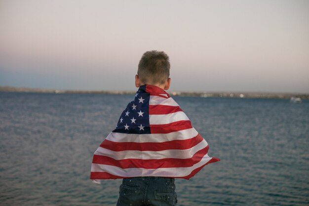 Little boy lets the american flag fly in his hands on the wind at the Sea
