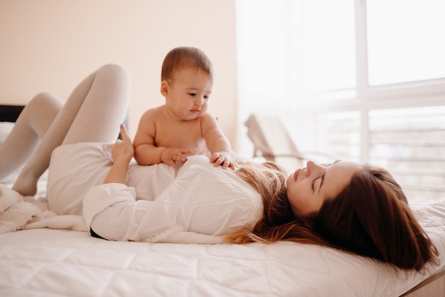 Little boy lies on his mom resting on the bed 