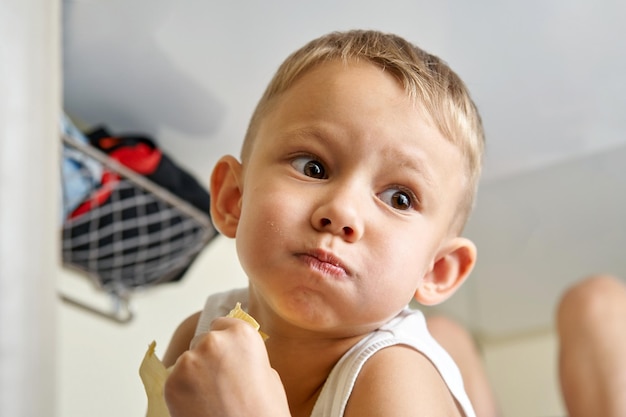 Little boy looks downward with doe eyes and mouth full of snacks chewing and holding sandwich