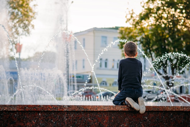 Foto il ragazzino esamina una fontana la sera soleggiata