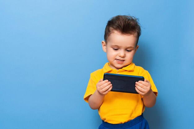 小さな男の子が携帯電話の画面を見る青い背景のスタジオ写真テキスト用のスペース