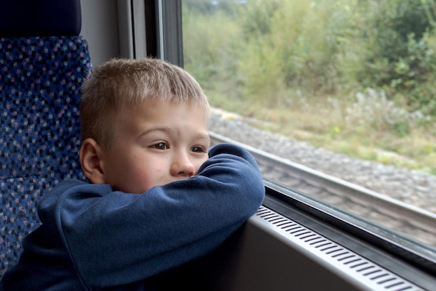 A little boy looks thoughtfully into the distance through the train window