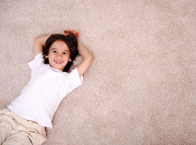 Little boy lying on carpet floor at home and smiling