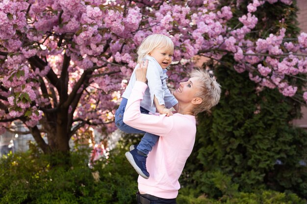 어린 소년과 어머니는 벚꽃이 만발한 정원에서 주말 활동을 하며 즐거운 시간을 보내고 있습니다. 봄 공원에서 자연 속에서 놀고 있는 엄마와 어린 아들