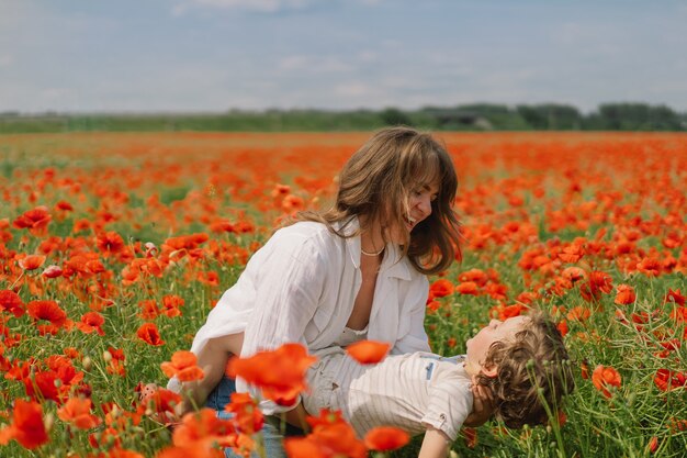 Little boy and mother is playing in a beautiful field of red poppies. 