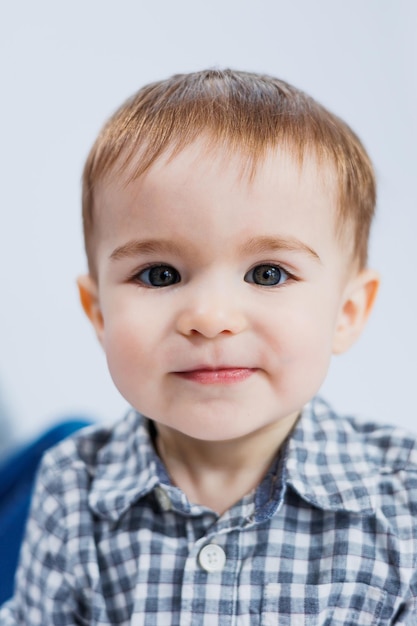 체크 무늬 셔츠를 입은 흰색 배경에 한 살 된 어린 소년 그의 얼굴에 미소를 가진 작은 아이