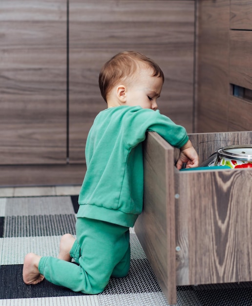 Little boy open the kitchen drawers to play with kitchenware inside Toddler boy in dangerous situation at home Child safety concept